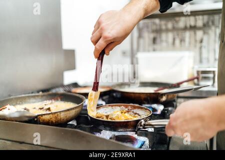 Crop unkenntlich Koch salzen und würzen Pfannen appetitlich Gerichte Vorbereitung auf Herd in der Restaurantküche Stockfoto