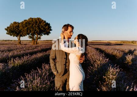 High-Winkel-Seitenansicht der romantischen neuvermählten Paar stehend Gesicht Auf dem weiten Feld gegen den violetten Sonnenuntergang Himmel zu blicken Stockfoto