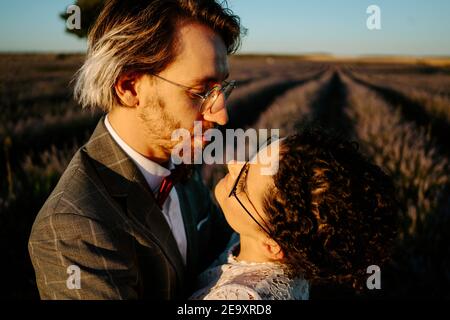 High-Winkel-Seitenansicht der romantischen neuvermählten Paar stehend Gesicht Auf dem weiten Feld gegen den violetten Sonnenuntergang Himmel zu blicken Stockfoto