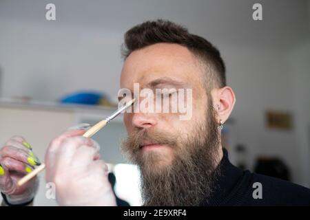 Nahaufnahme eines unkenntlichen Make-up-Künstlers, der ein Make-up aufsetzt Das Gesicht des Hipster-Mannes Stockfoto