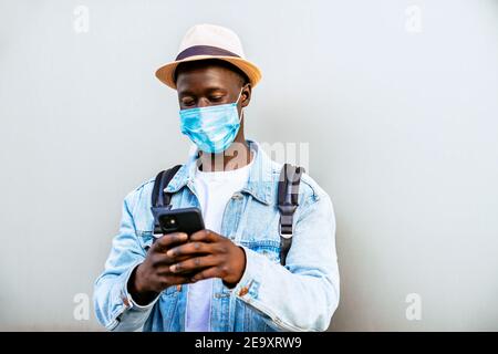 Anonymer ethnischer Mann mit Hut und Gesichtsmaske Messaging auf Handy auf hellem Hintergrund Stockfoto