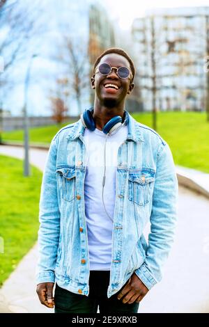 Junger afroamerikanischer Mann in Denim-Jacke mit Kopfhörern Auf dem Weg zwischen den Rasenflächen in der Stadt Stockfoto