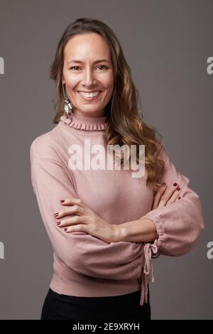 Porträt einer glücklichen, eleganten, reifen Geschäftsfrau, die mit gekreuzten Armen im Studio steht und die Kamera anschaut Stockfoto