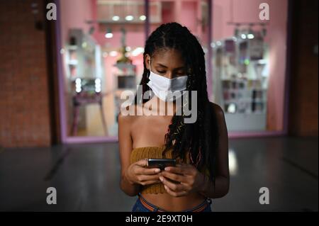 Porträt einer attraktiven jungen afro-lateinischen Frau mit Gesichtsmask und Smartphone in einem Einkaufszentrum in Kolumbien Stockfoto