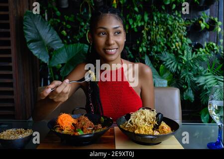 Portrait einer attraktiven jungen Afro Latina mit Dreadlocks in einem gehäkelten roten Top Essen im asiatischen Restaurant, Kolumbien Stockfoto
