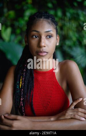 Porträt einer besinnlichen jungen Afro Latina mit Dreadlocks in einer gehäkelten roten Tischplatte auf dem Tisch sitzend, Kolumbien Stockfoto