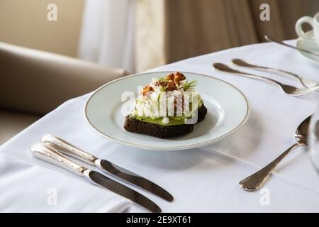 Von oben von gesunden Avocado Toast mit Ricotta und Walnüssen Auf weißem Teller und auf dem Tisch im Café serviert Während des Frühstücks Stockfoto