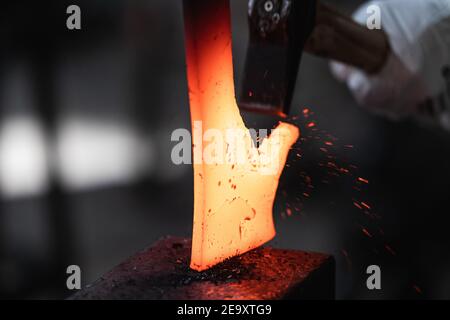 Unerkennbarer Handwerker hämmert während des Schmiedens heißes Eisenstück auf Amboss Prozess in der Werkstatt Stockfoto