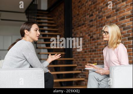 Nachdenkliche junge Frau auf der Therapiesitzung, eine weibliche Beraterin mittleren Alters, die mit Aufmerksamkeit und Empathie zuhört Stockfoto