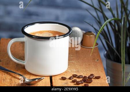 Eine weiße Kaffeetasse mit cremefarbenem Kaffee steht auf einer farbigen hölzernen Oberfläche. Kaffeebohnen sind daneben Stockfoto