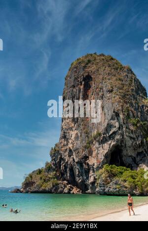 Eine riesige Felsformation überschattet den weißen Sand und das blaue Meer des Railay Beach in Krabi, Thailand Stockfoto