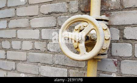 Gelbes Gasventil an der Rohrleitung entlang der Gebäudewand. Stockfoto