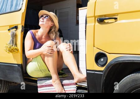 Junge blonde Frau, die mit dem Wohnmobil am Meer unterwegs ist. Selbst gebaute Off-Grid Wohnmobil am Strand geparkt. Stockfoto