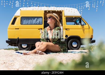 Junge blonde Frau, die mit dem Wohnmobil am Meer unterwegs ist. Selbst gebaute Off-Grid Wohnmobil am Strand geparkt. Stockfoto