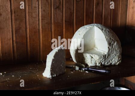 Stillleben mit Bauernkäse und einem Messer auf rustikalem Holzhintergrund. Stockfoto