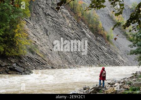 Frau im roten Mantel, die am Ufer des tiefen Flusses Prut in Jaremche, Ukraine, steht. Stockfoto