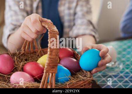 Nahaufnahme des Kindes, das farbige Eier in den Korb legt und vorbereitet Für Osterferien Stockfoto