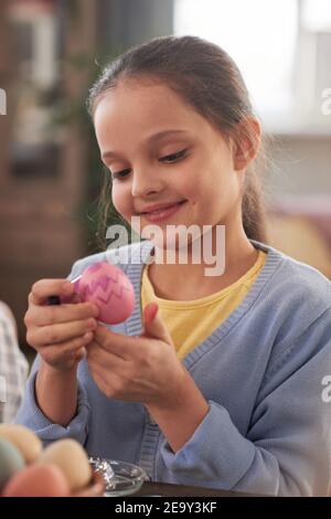 Kleines Mädchen Blick auf Osterei in ihren Händen sie Malen Sie es für den Urlaub Stockfoto