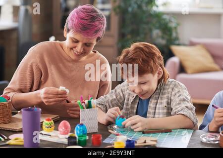 Junge Frau, die zusammen mit Jungen und am Tisch sitzt Malen von Eiern mit Farben für Ostern Stockfoto