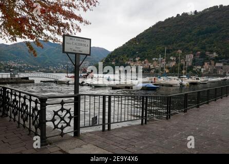 COMO, LOMBARDEI, ITALIEN - 06. November 2019: Diga Piero Foranea Caldirola Pier Schild am Comer See in tiefen Herbstlandschaft mit roten Blättern, Eisenzaun A Stockfoto