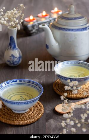 Draufsicht auf zwei Tassen chinesischen Tee, blaue Teekanne, Vase, weiße Blumen und Kerzen, mit selektivem Fokus, auf dunklem Tisch, in vertikaler Richtung Stockfoto