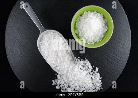 Kleine Porzellanschüssel und Messlöffel voll Meersalz auf Schwarze Schale Stockfoto