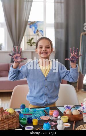 Portrait von kleinen Mädchen lächelt an der Kamera während der Malerei Ostern Eier mit Farben am Tisch zu Hause Stockfoto