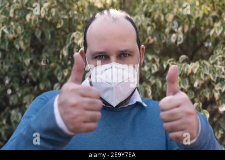 Wirksamer Schutz vor ansteckenden Krankheiten. Der Mann zeigt Daumen nach oben und trägt eine hygienische Maske, um Infektionen, Atemwegserkrankungen wie Grippe zu verhindern Stockfoto