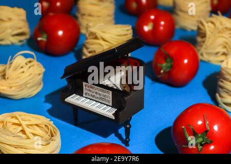 Spielzeugflügel zwischen Nudelnestern und reifen Tomaten in Reihen vor hellem azurblauem Hintergrund, absurdes Food-Foto gestapelt Stockfoto