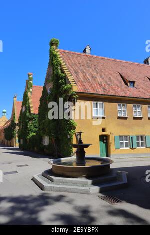 DEUTSCHLAND, AUGSBURG - 18. AUGUST 2019: Gebäude und Brunnen in der Fuggerei in Augsburg Stockfoto