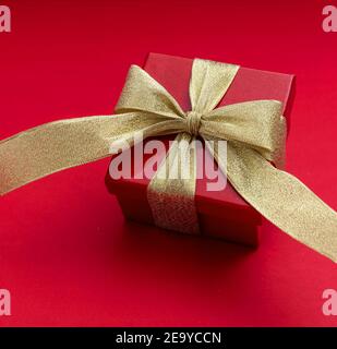 Geschenkbox mit Goldband auf rotem Hintergrund. Glänzende Paket valentinstag Geschenk, weihnachten und Jubiläum Feier, Stockfoto