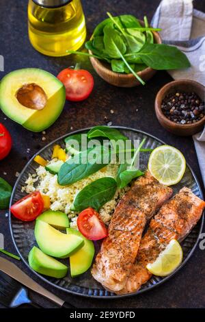 Gegrilltes Lachsfilet mit Couscous, Salat frisches Gemüse und Avocado auf dunklem Hintergrund. Stockfoto