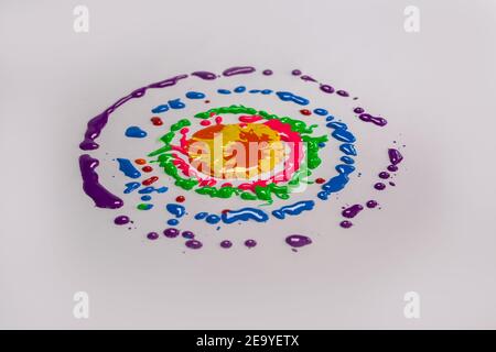 Farben fallen auf einen sich drehenden weißen Hintergrund. Die Farbe der Tropfen ist ein kreisförmiger Halo Stockfoto