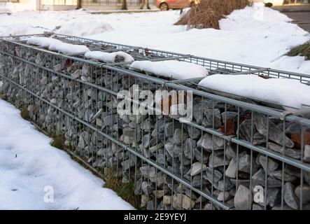 Trennung der Straße vom Parkgelände. Ein Fragment der Raumordnung mit der Verwendung von Gabionen. Winter. Stockfoto