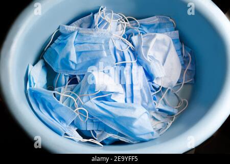Draufsicht auf viele gestapelte medizinische blaue Masken. Viele gebrauchte zerknitterte medizinische Schutzmasken auf blauem Hintergrund. Blick von oben. Ovales Becken Stockfoto