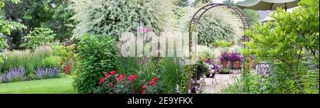 Magische japanische Weiden Zierbäume in einem Sommergarten umgeben von einer Rosen, Karl Foerster Feather Reed Gras, Minze, Federgras in Chicago Stockfoto