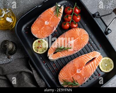 Drei rohe frische Steak Fisch Forelle, Lachs und Gewürze auf der Grillpfanne, Blick von oben Stockfoto