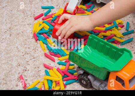 Kinderspiel bestehend aus in verschiedenen Farben bemalten Nudeln und ein Spielzeug-LKW. Kinderspiele. Entwicklung von Kindern. Taktile Babyspiele Stockfoto