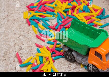 Kinderspiel bestehend aus in verschiedenen Farben bemalten Nudeln und ein Spielzeug-LKW. Kinderspiele. Entwicklung von Kindern. Taktile Babyspiele Stockfoto