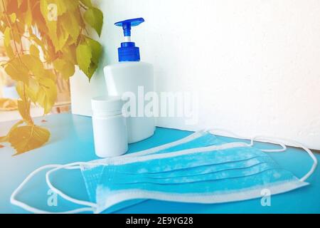 Eine Flasche mit einem Antiseptikum und ein Glas Medikamente, steht neben dem Fenster vor einem Hintergrund von grünen Blättern und einem weißen Hintergrund mit Masken, hyg Stockfoto