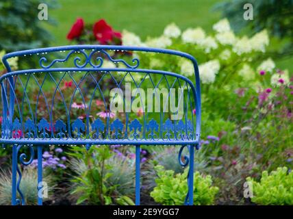 Vintage blaue Gartenbank in einem monet-ähnlichen Garten nach einem Regensturm. Stockfoto