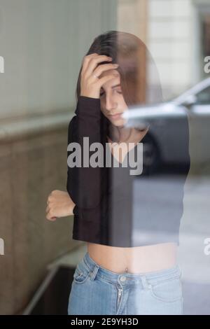 Vertikales Porträt einer schönen jungen Frau auf der gegenüberliegenden Seite Seite des Fensters Stockfoto