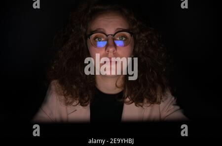 Frau, die nachts mit dem Computer arbeitet und den Bildschirm in ihrer Brille reflektiert. Frau ist müde, Überarbeit Konzept. Stockfoto