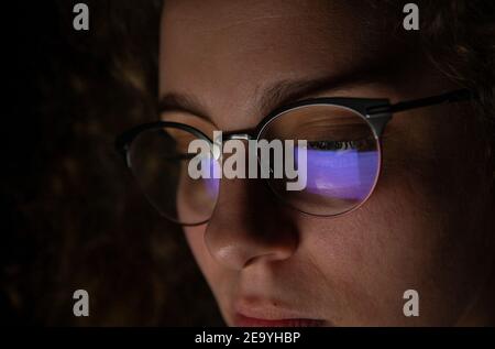 Spiegelung eines Computerbildschirms in der Brille einer Frau, die nachts arbeitet. Programmierer oder Entwickler. Stockfoto