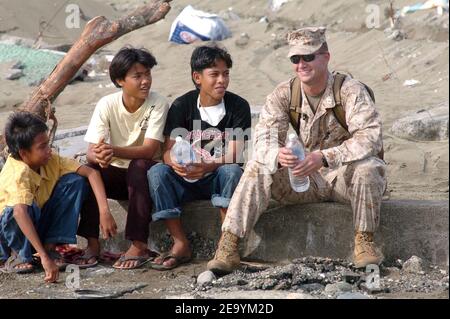 Marine Capt. Jamey Stover, der Marine Expeditionary Unit (MEU) von 15th zugeordnet, sitzt mit lokalen indonesischen Kindern zusammen, während Matrosen und Marines die Versorgung von einem Landing Craft Air Cushion (LCAC) abladen. Die LCACs der Assault Craft Unit Five (ACU-5) sind der USS Bonhomme Richard (LHD 6) Expeditionary Strike Group zugeordnet, die derzeit im Indischen Ozean vor den Gewässern Indonesiens und Thailands zur Unterstützung der Operation Unified Assistance tätig ist, Die humanitäre Operation nach dem Tsunami, der Südostasien am 11. Januar 2005 heimsuchte. Foto von Alan D. Monyelle/USN/ABACA Stockfoto