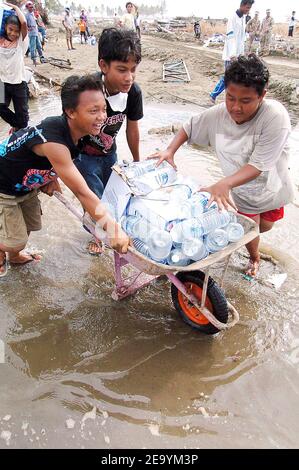 Indonesische Kinder tragen in einer Schubkarre Flaschen mit Trinkwasser, nachdem sie es von US-Matrosen und Marines erhalten haben, die Hilfsgüter von einem Landing Craft Air Cushion (LCAC), 11. Januar 2005 in Meulaboh, Sumatra, Indonesien, abgeladen haben. Die LCACs der Assault Craft Unit Five (ACU-5) sind der USS Bonhomme Richard (LHD 6) Expeditionary Strike Group zugeordnet, die derzeit im Indischen Ozean vor den Gewässern Indonesiens und Thailands zur Unterstützung der Operation Unified Assistance tätig ist, Die humanitäre Operation im Gefolge des Tsunamis, der Südostasien getroffen hat. Foto von Alan D. Moyelle/USN Stockfoto
