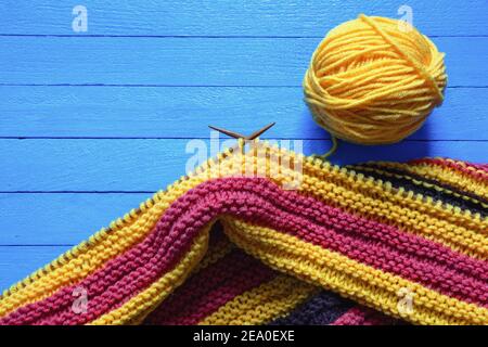 Hobbys-Konzept. Hell gestreiftes Stricktuch mit Stricknadeln und Wollkugel auf blauem rustikalem Tisch. Speicherplatz kopieren Stockfoto