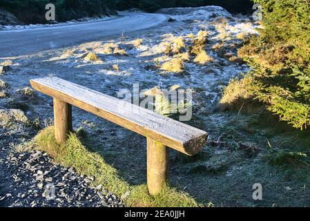 Schöne Aussicht auf eine kleine Holzbank bedeckt mit Frost neben der Straße in Ticknock National Forest Park, Co. Dublin, Irland Stockfoto