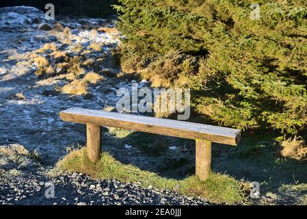 Schöne Aussicht auf eine kleine Holzbank bedeckt mit Frost neben der Straße in Ticknock National Forest Park, Co. Dublin, Irland Stockfoto