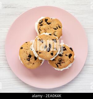 Hausgemachte Schokolade Chip Cookie Ice Cream Sandwich auf einem rosa Teller auf einer weißen Holzoberfläche, Draufsicht. Über Kopf, von oben, flach liegend. Stockfoto